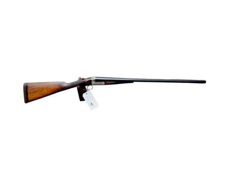 Side view of a wooden-stock shotgun with a long metal barrel, lying horizontally with a price tag hanging from the trigger guard