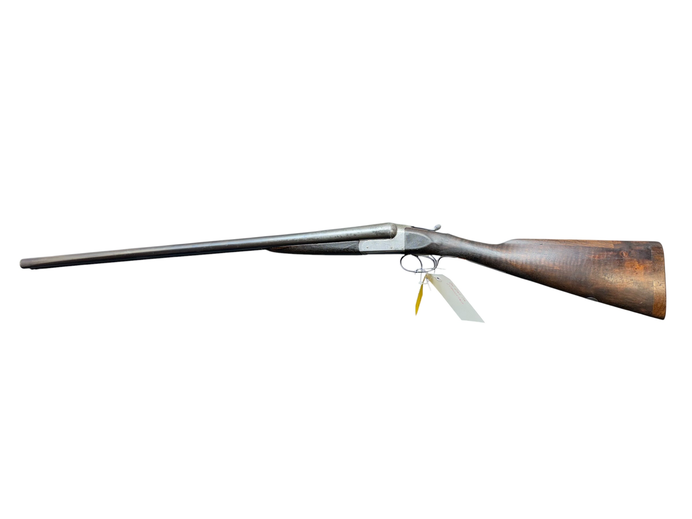 IMG_5314-Photoroom - OWS-Ammo Side view of a classic double-barrel shotgun with wooden stock and two triggers, laid on its side against a white background, with a tag attached beneath the stock