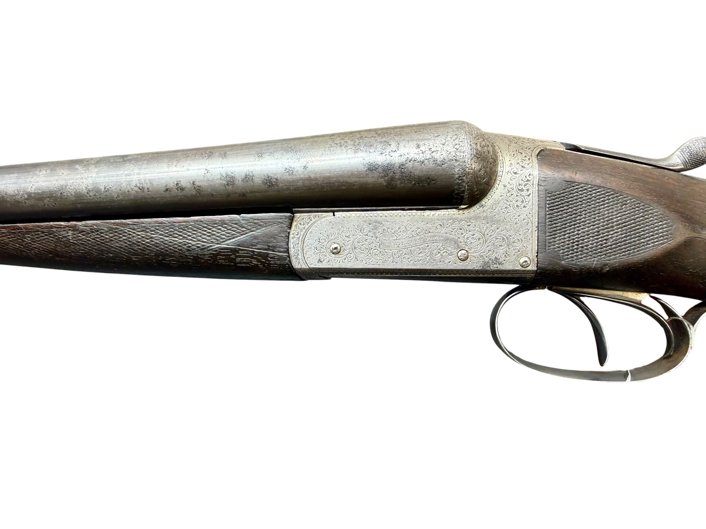 IMG_5317-Photoroom - OWS-Ammo Close-up of an antique engraved shotgun side with ornate silver receiver and two triggers visible against a white background