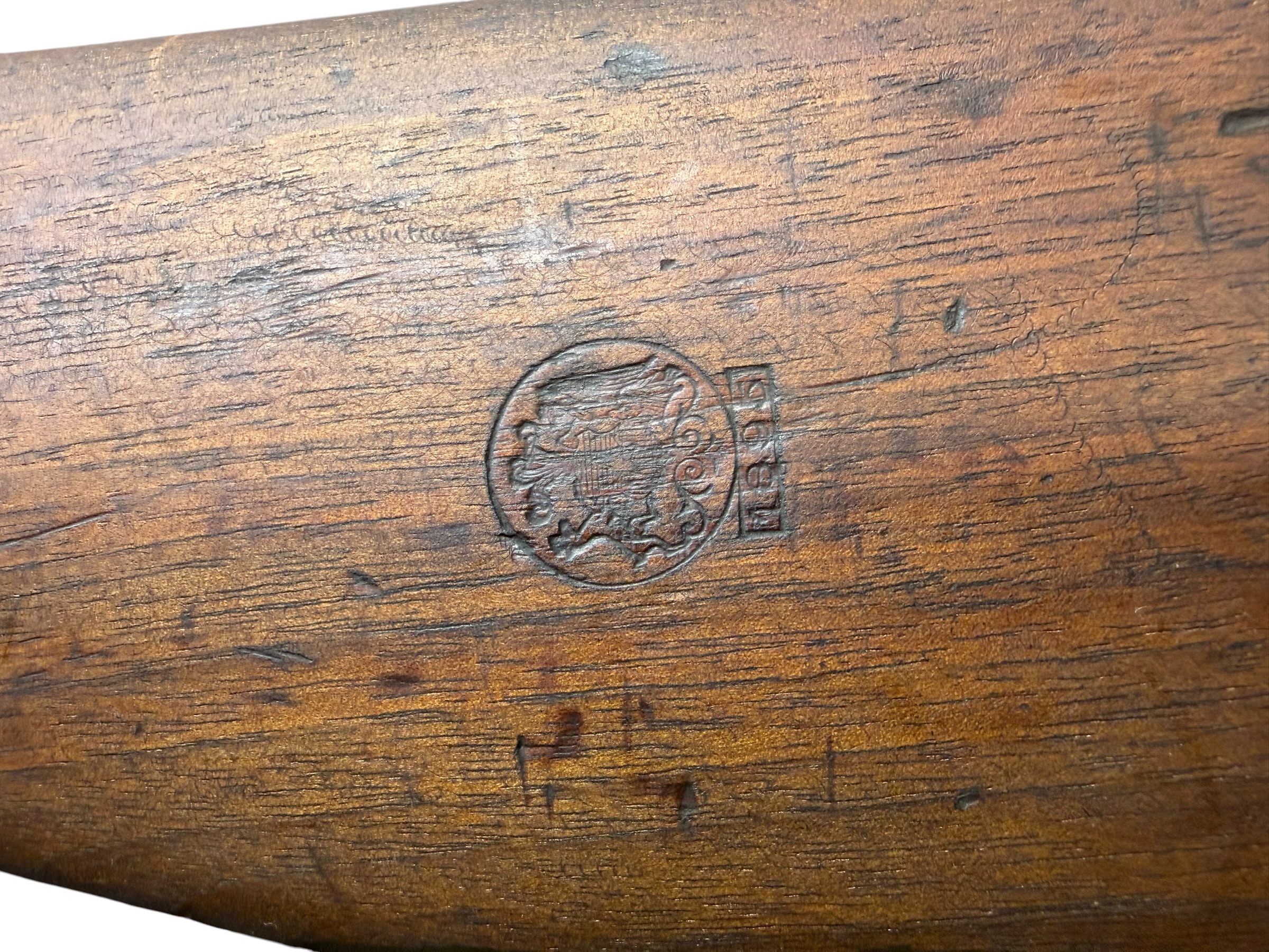 IMG_5329-Photoroom - OWS-Ammo Close-up of a dark, worn wooden surface with prominent grain and a circular stamped mark.