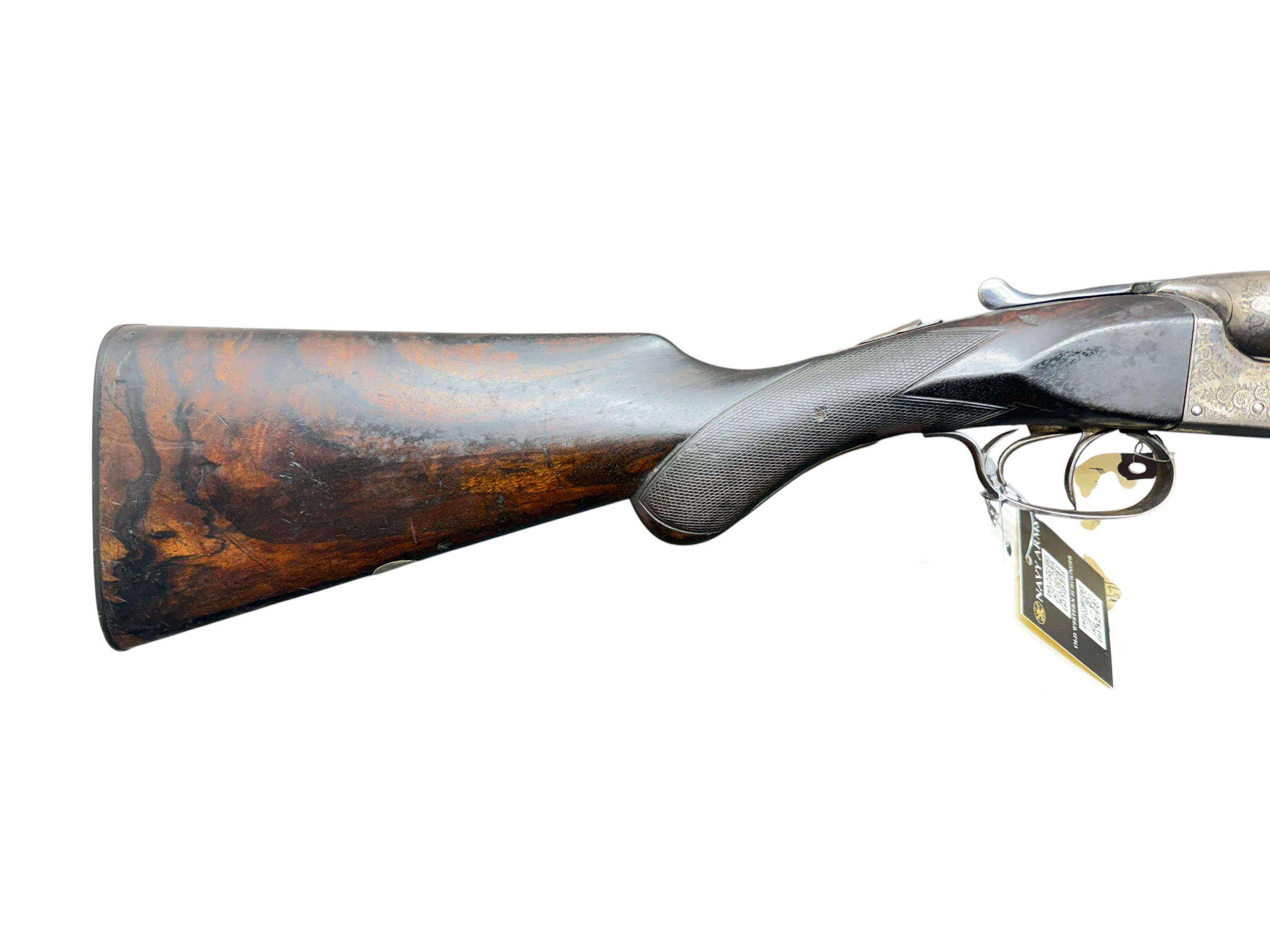 IMG_5379-Photoroom - OWS-Ammo Side view of a double-barreled shotgun with a rusted, wooden stock and engraved metal receiver; blade triggers visible and a tag hanging near the trigger guard.