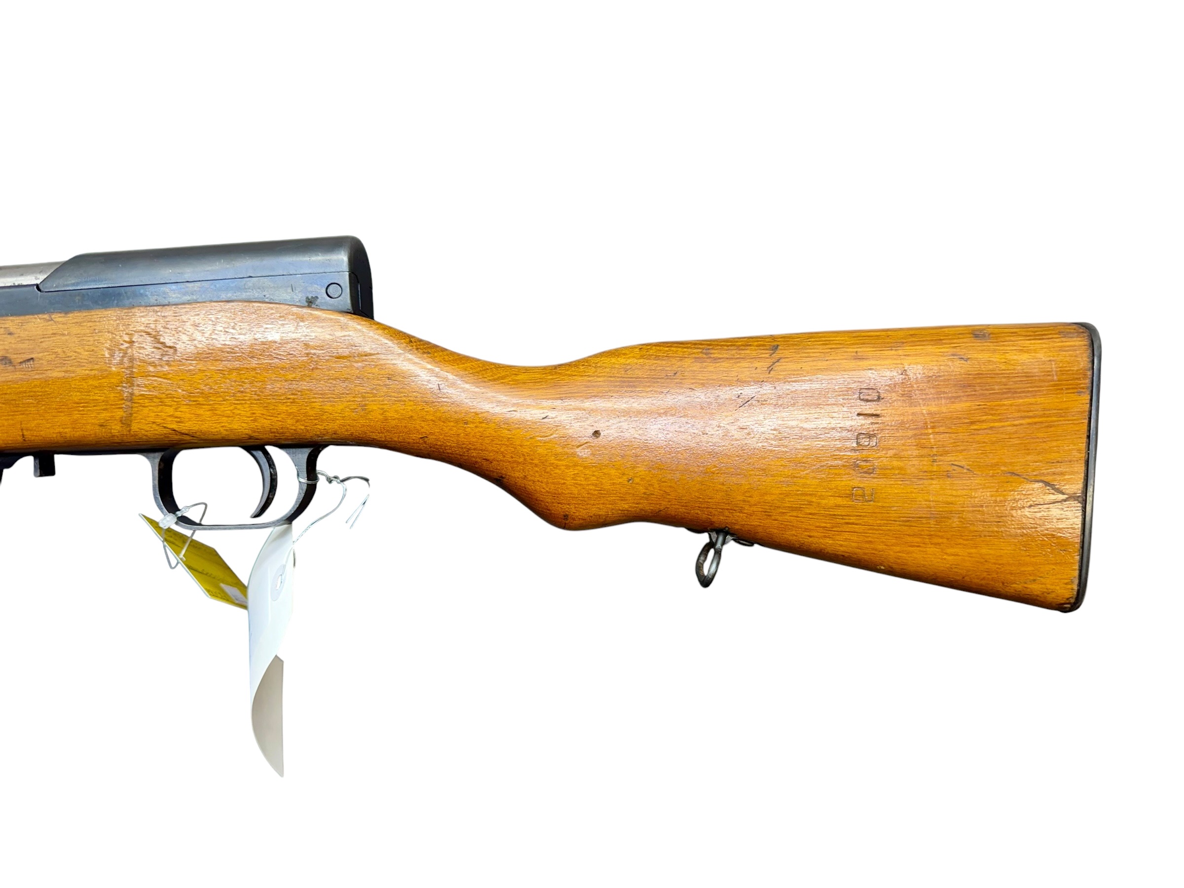 Close-up of a wooden rifle stock with metal receiver and a hanging tag nearby.