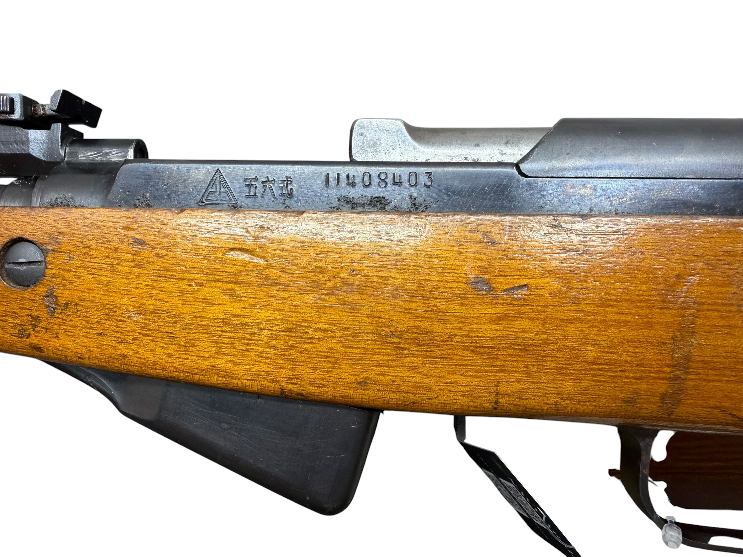 Close-up of a bolt-action rifle's metal receiver with a triangle crest, serial-like digits, and a wooden stock.