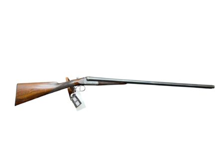 Side view of a hunting shotgun with a wooden stock and long metal barrel, a tag hanging from the trigger guard.